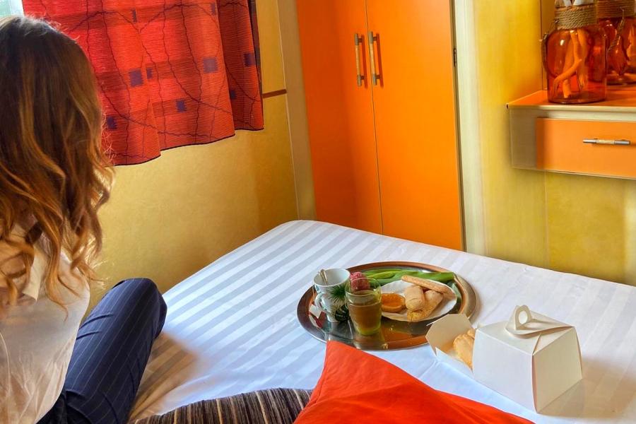 Camera colorata con colazione sul letto, donna guarda fuori dalla finestra.