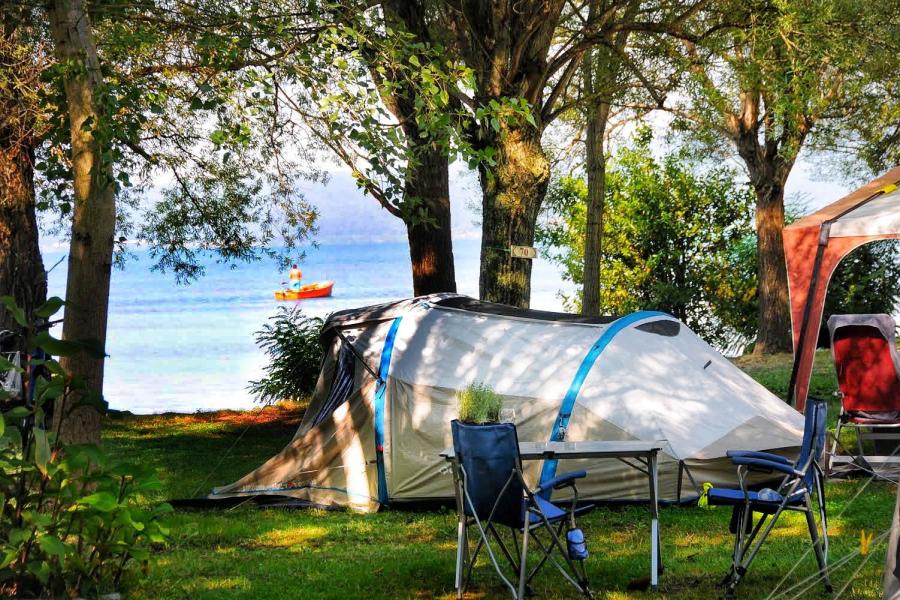 Camping by the lake with a tent, chairs, and a boat in the distance.
